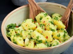 a bowl filled with potatoes and parsley on top of a black table next to two wooden spoons