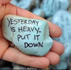 a hand holding a rock with writing on it that says, yesterday is heavy put it down