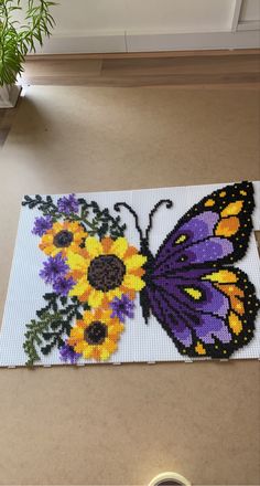 a cross - stitch butterfly and sunflowers is on the floor next to a potted plant