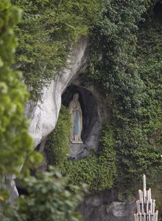 there is a statue in the middle of some trees and bushes on the side of a mountain