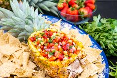 a pineapple is topped with fruit and salsa surrounded by chips on a blue plate