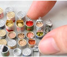 a hand is pointing at some miniature food in small cans and spoons on the table