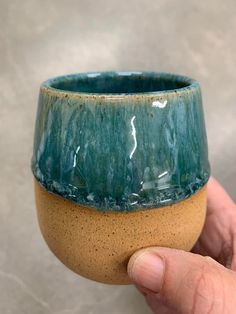 a hand holding a green and brown ceramic cup in it's left hand on a gray background