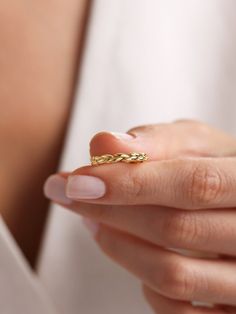 a woman's hand holding a gold ring in her left hand and wearing a white shirt