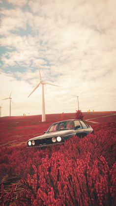 a car is parked in the middle of a field with wind turbines behind it and red flowers