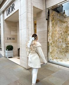 a woman is walking down the sidewalk in front of a dior store with her back to the camera