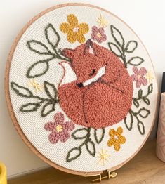 a close up of a embroidery on a wooden table with a clock and vase in the background