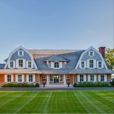 a large house with two story windows and white trim on the roof, surrounded by lush green grass