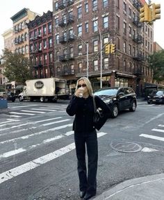 a woman standing in the middle of an intersection with cars and buildings on both sides