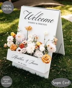 a welcome sign with flowers on it sitting in the grass