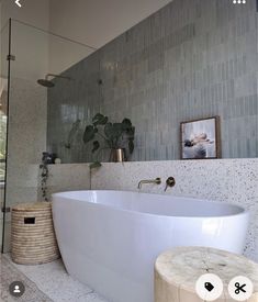 a large white bath tub sitting in a bathroom next to a wooden stool and potted plant