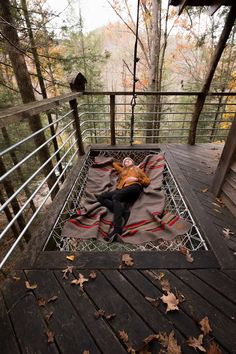 a man laying on top of a blanket in the middle of a wooden deck surrounded by trees