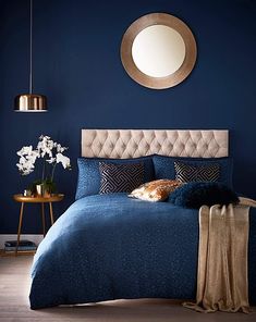 a bed with blue sheets and pillows in front of a round mirror on the wall