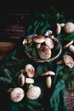 some nuts are in a glass bowl on a green table cloth with pine cones and needles