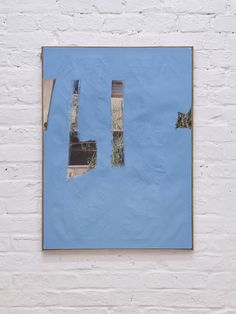 a painting hanging on the side of a white brick wall in front of a blue sky