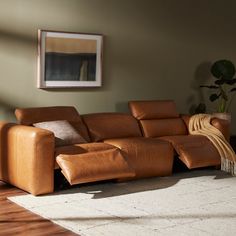 a brown leather couch sitting on top of a hard wood floor next to a window