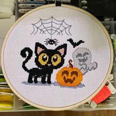 a cross - stitch halloween scene with a black cat and pumpkin