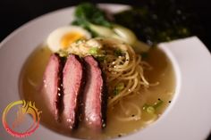 a white plate topped with meat, noodles and broccoli next to an egg