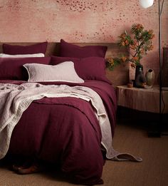 a bed with red linens and pillows in a pink room next to a lamp