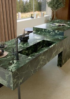 a green marbled counter top with two sinks in front of a large window,