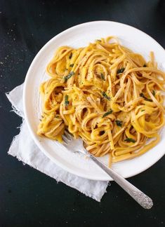 a white plate topped with pasta covered in sauce and parsley next to a fork