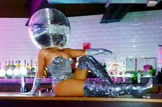 a woman sitting on top of a bar wearing silver sequins and holding a disco ball