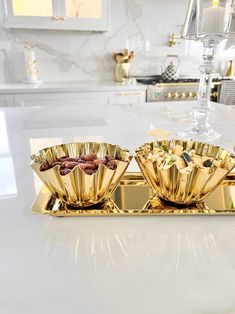 three golden bowls filled with food on top of a white counter