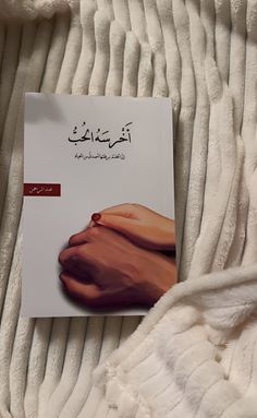 an open book with arabic writing on top of a white bed spread and two hands touching each other's fingers