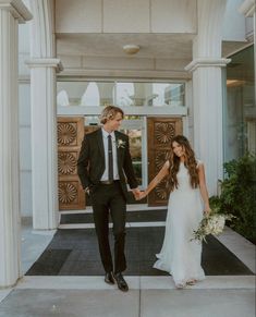 a bride and groom are holding hands in front of the entrance to their wedding venue