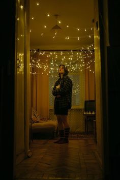 a woman is standing in the doorway with her arms crossed and lights strung all around her