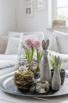 two bunny statues sitting on top of a table next to plants and eggs in a glass vase