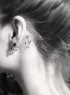 a woman's ear has a small flower tattoo on it, behind her ear