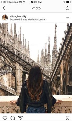 a woman standing on top of a balcony next to an old building and looking at the sky