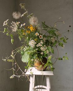 a vase filled with lots of flowers sitting on top of a white table next to a wall