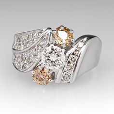 This lovely three-stone diamond ring is centered with one (1) round brilliant cut diamond set into a six- prong setting and flanked to each side by one (1) old European cut fancy light brown colored diamond set into a six-prong setting. The shoulders of the ring are accented with diamonds. One shoulder is bead set with nineteen (19) round single cut diamonds and one (1) round brilliant cut diamond. The other shoulder is channel set with five (5) round brilliant cut diamonds. The ring measures 13.1mm at the top, rises 6.8mm above the finger, tapering to 2.9mm wide and 1.1mm thick at the base of the shank. It is currently a size 6. Several of the diamonds are lightly chipped. Classic Brown Diamond Jewelry, Brown Diamond Ring With Diamond Accents For Anniversary, Brown Diamond Ring With Accents For Anniversary, Anniversary Brown Diamond Ring With Accents, Brown Diamond Anniversary Ring, Brown Prong-set Ring For Anniversary, Brown Prong Set Ring For Anniversary, Brown Rings With Prong Setting For Anniversary, Brown Diamond Jewelry For Anniversary