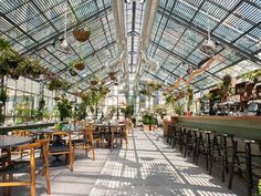 the inside of a greenhouse with tables and chairs, potted plants and hanging lights