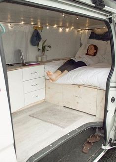 a woman laying on top of a bed in the back of a white van with its door open