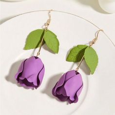 two purple flowers with green leaves hanging from gold earwires on a white plate