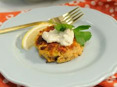 a white plate topped with crab cakes covered in sour cream and garnished with parsley