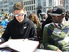 two young men sitting at a table with papers and pens in front of them,