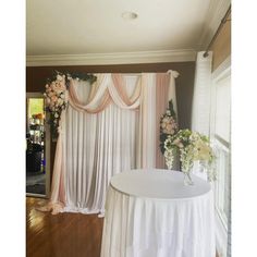 a white table topped with a vase filled with flowers sitting next to a window covered in drapes