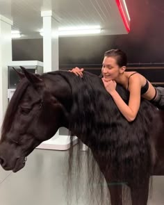 a woman sitting on the back of a black horse in a showroom with long hair