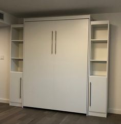 an empty room with white cupboards and shelving unit in the center, on hard wood flooring