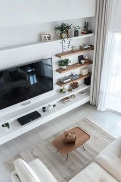 a living room with white furniture and a flat screen tv mounted on the wall above it