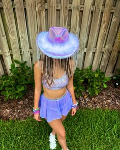 a woman wearing a purple hat and skirt in front of a fence