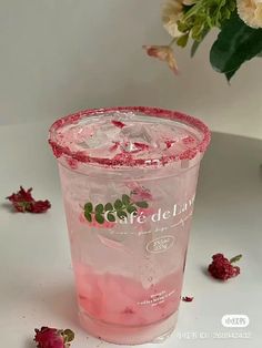 a pink drink in a plastic cup with ice and strawberries on the table next to it