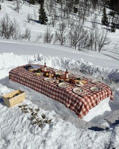 a picnic table set up in the snow with plates on it and food spread out