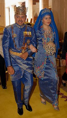 two people dressed in blue and gold walking down a yellow carpeted hall with other people