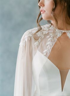 the back of a woman's white dress with long sleeves and flowers on it