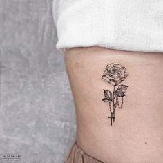 a rose tattoo on the side of a woman's ribcage, with a cross